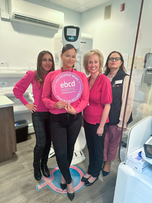 Women at a mammogram unit holding an Enhanced Breast Cancer Detection (EBCD) sign